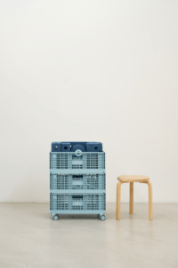 Three blue MODU crates stacked on castor wheels beside a wooden stool, with blue modular blocks in the top crate.
