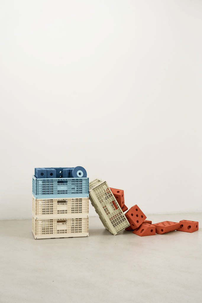 Blue and cream MODU crates stacked beside a tilted sage-green crate, with orange modular blocks scattered across the floor.