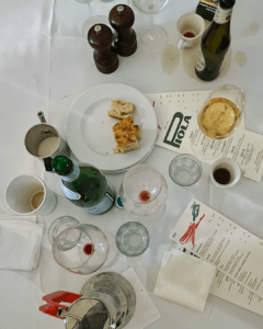Piola menus among wine glasses, espresso cups, bottles and bread on a white tablecloth marked with spills.