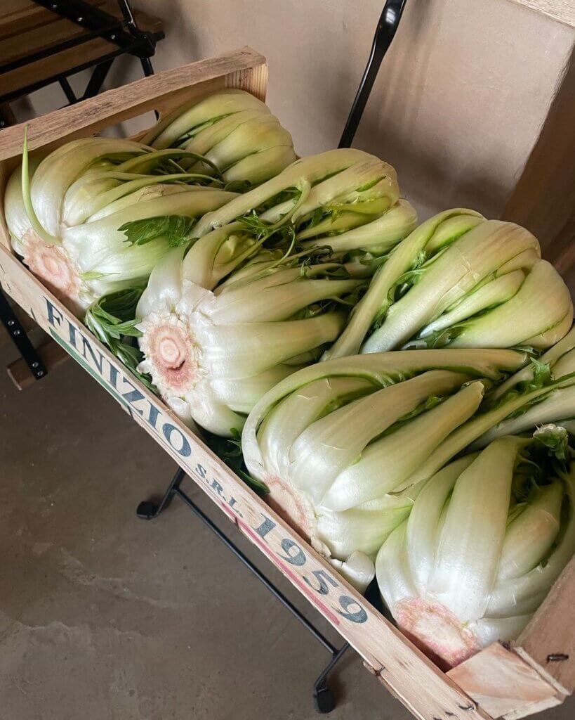 A wooden crate of fresh green vegetables resting on a chair inside the restaurant.