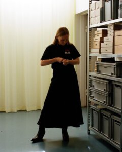 Tine, Tourell’s founder, standing beside shelves of storage boxes in her office, looking down at her hands.