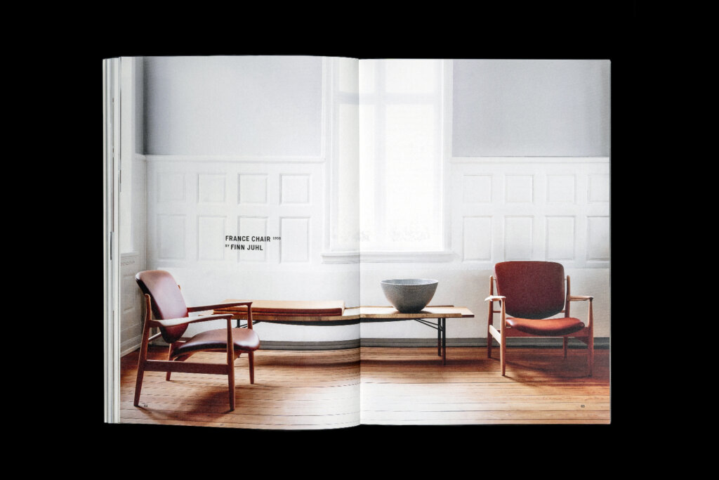 House of Finn Juhl catalogue spread showing two red lounge chairs and a low table in a bright room with tall windows.