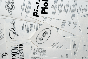 Overlapping Piola menus combining flowing scripts, bold rounded lettering and condensed type in black on white paper.