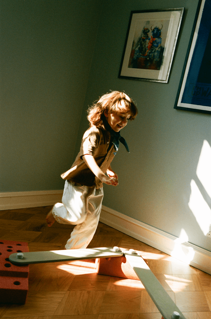 A child runs beside pale green MODU beams on orange-coloured blocks in a room with green walls and strong sunlight across the floor.