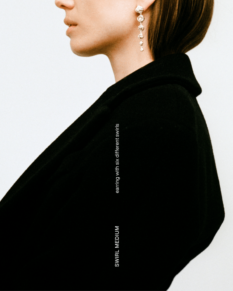 Cropped profile of a model in black wearing a dangling earring. Text reads “SWIRL MEDIUM” and “earring with six different swirls.”