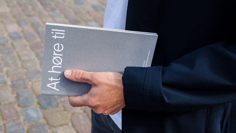 The silver At Høre Til catalogue held in a hand